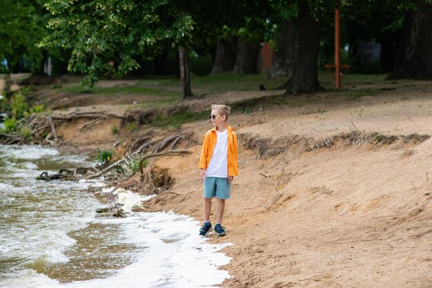 Un niño con una camisa naranja en la orilla del mar.