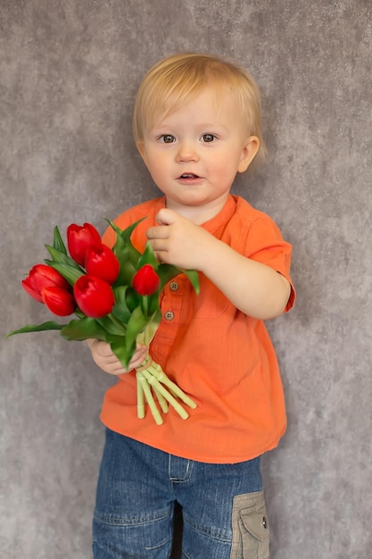 Un niño con una camisa naranja y vaqueros sostiene tulipanes rojos en racimos