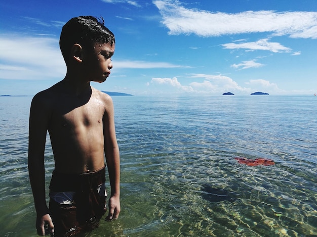 Foto niño sin camisa de pie en el mar contra el cielo