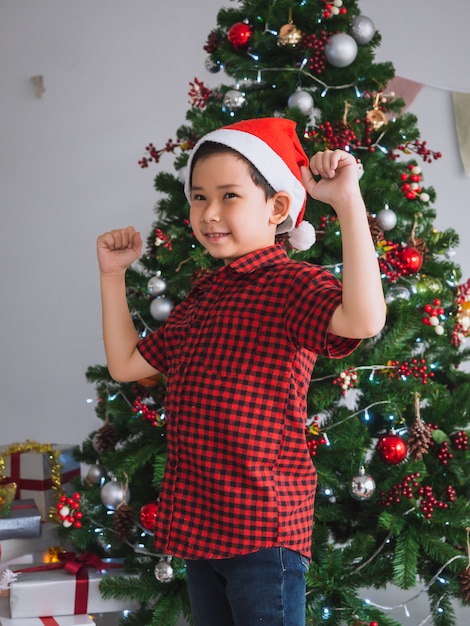 Foto niño con camisa roja es feliz y divertido para celebrar la navidad con el árbol de navidad