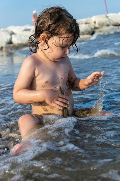 Niño sin camisa sentado en la playa