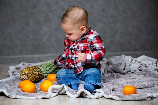 El niño de la camisa se sienta en el plaid y sostiene la fruta.