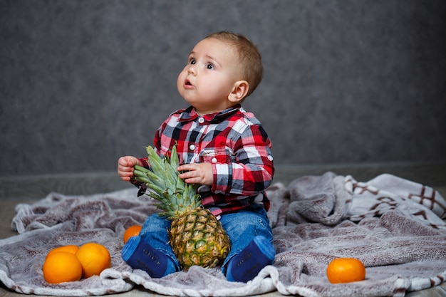 El niño de la camisa se sienta en el plaid y sostiene la fruta.