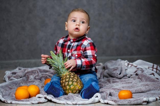 El niño de la camisa se sienta en el plaid y sostiene la fruta.