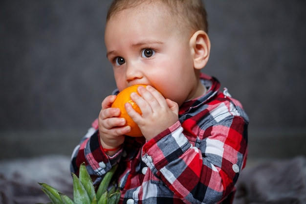 El niño de la camisa se sienta en el plaid y sostiene la fruta.