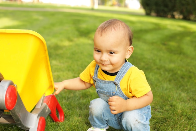 Un niño con una camiseta amarilla de cb está sentado en el césped del parque junto a un carro con