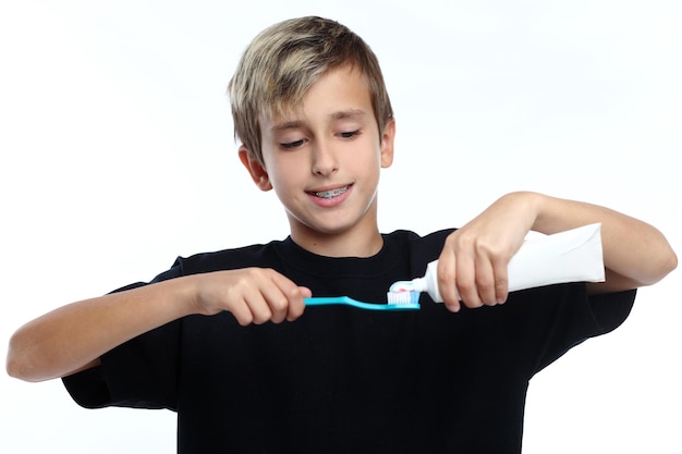 Niño con camiseta blanca aprieta la pasta de dientes en el cepillo y se prepara para cepillarse los dientes