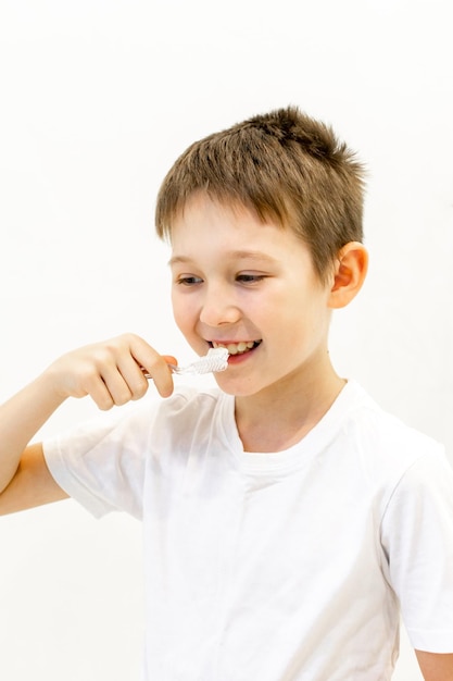 Un niño con una camiseta blanca se cepilla los dientes en el baño. Foto de alta calidad