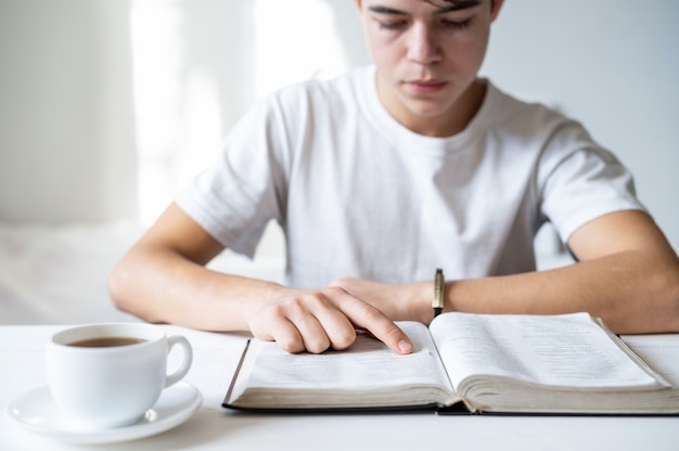 Un niño con camiseta blanca leyendo un libro sobre la mesa, taza de café cerca del libro