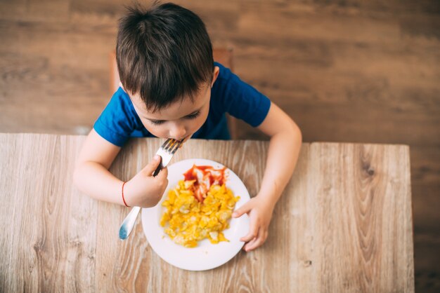 Foto un niño con una camiseta en la cocina comiendo una tortilla, tenedor