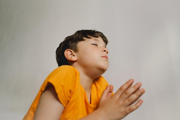 Un niño con una camiseta naranja reza en casa concepto de la fe
