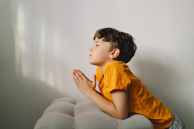 Foto un niño con una camiseta naranja reza en casa concepto de fe