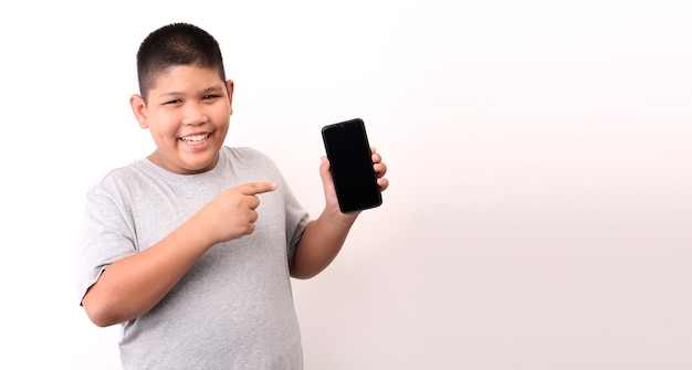 Foto niño en camiseta que presenta teléfono inteligente sobre fondo blanco en estudio.