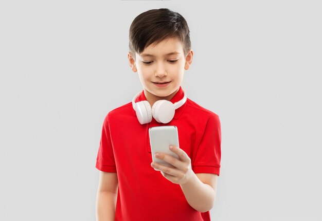 Foto niño con camiseta roja con auriculares y teléfono inteligente