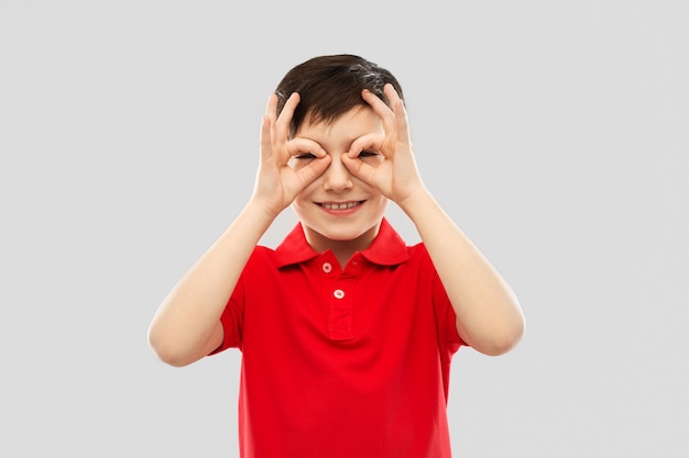 niño con camiseta roja mirando a través de gafas de dedos
