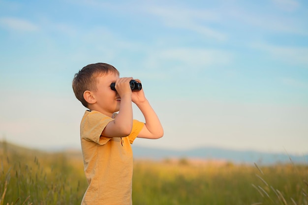 un niño se para en un campo y mira a través de binoculares