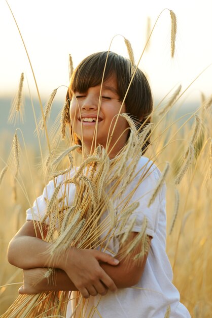 Niño en el campo de trigo abrazando el grano de la cosecha