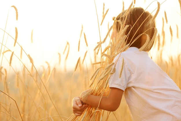 Niño en el campo de trigo abrazando el grano de la cosecha