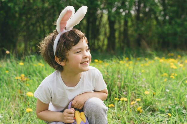 Niño con canasta de huevos y orejas de conejo en la caza de huevos de Pascua en el jardín soleado de primavera