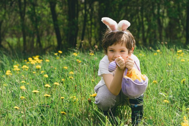 Niño con canasta de huevos y orejas de conejo en la caza de huevos de Pascua en el jardín soleado de primavera