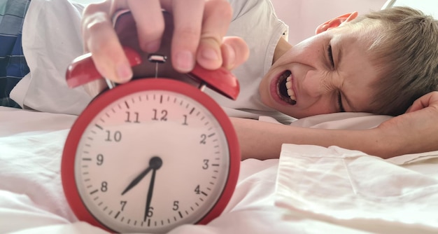 Foto niño cansado estresado durmiendo en la cama con un despertador