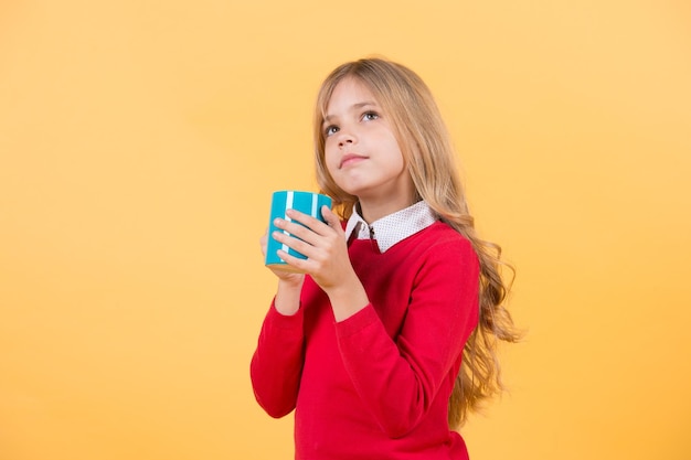 Niño con cara pensante sostenga una taza azul sobre fondo naranja