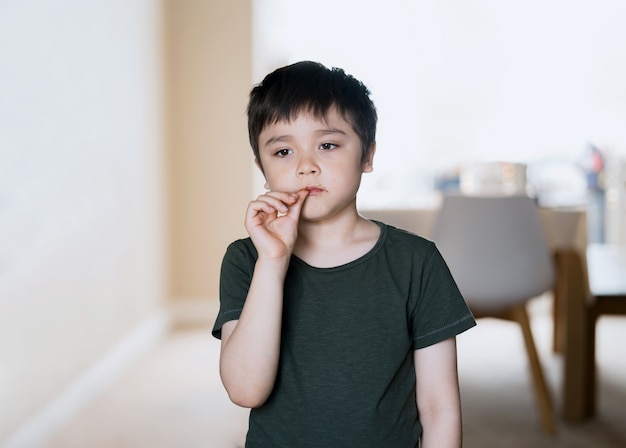 Niño con cara sucia de chocolate poniéndose golpe en la boca, retrato de clave alta El niño disfruta comiendo pastel de chocolate y lamiendo el dedo, Niño de pie en la sala y mirando profundamente