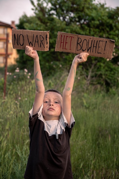 Un niño con la cara sucia y los ojos tristes sostiene un cartel de cartón con la inscripción NO HAY GUERRA