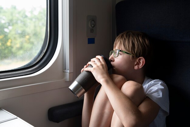 Niño en el carro del compartimento está bebiendo té y mirando por la ventana