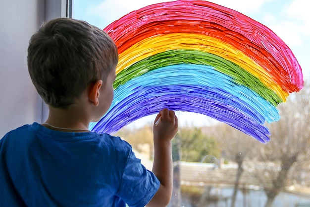 Niño en casa dibuja un arco iris en la ventana Comunidad de la sociedad Flash mob en cuarentena de autoaislamiento