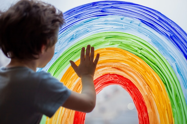 Foto niño en casa dibuja un arcoiris en la ventana.