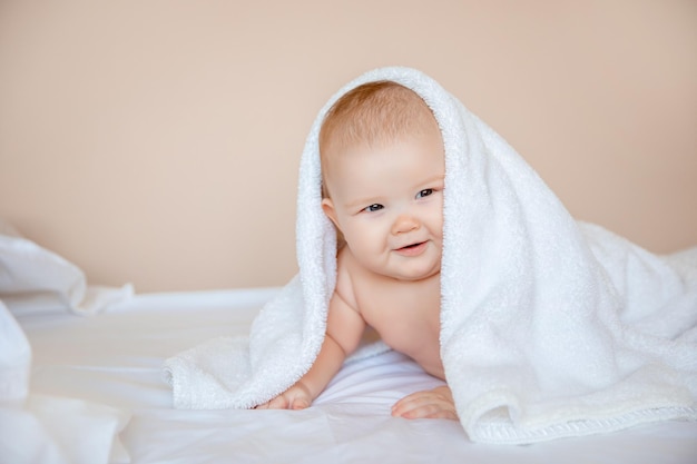 niño en casa en el dormitorio acostado en una sábana blanca envuelta en una toalla después de bañarse