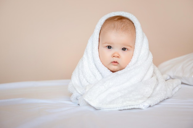 niño en casa en el dormitorio acostado en una sábana blanca envuelta en una toalla después de bañarse