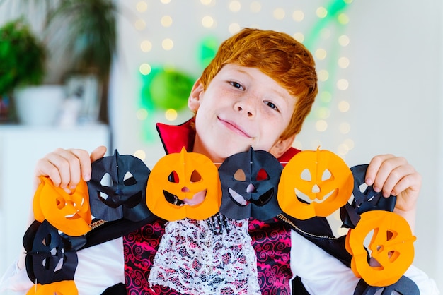 Niño en casa vestido como un vampiro para la fiesta de disfraces de Halloween jugando con decoración de calabaza