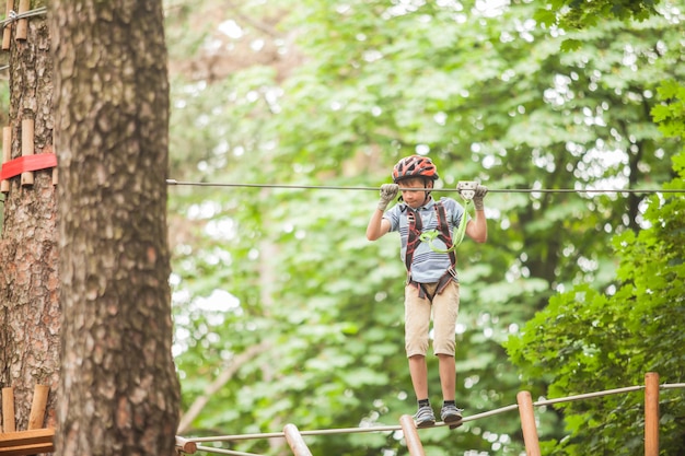 Un niño con un casco y equipo de seguridad en el parque de cuerdas de aventura en el fondo de la naturaleza.