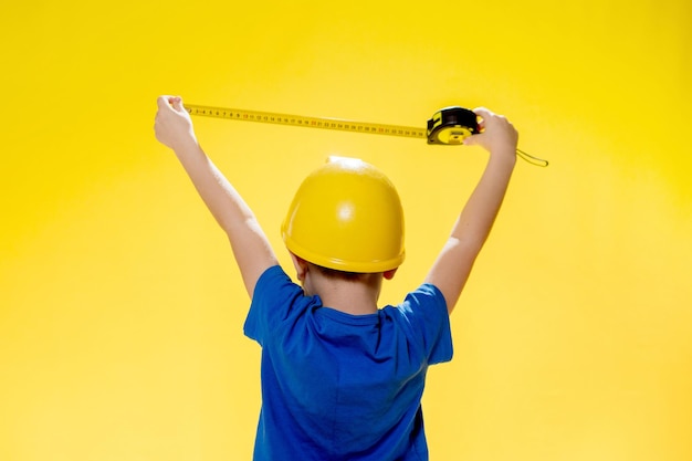 Un niño con un casco de protección de construcción mide con una cinta métrica