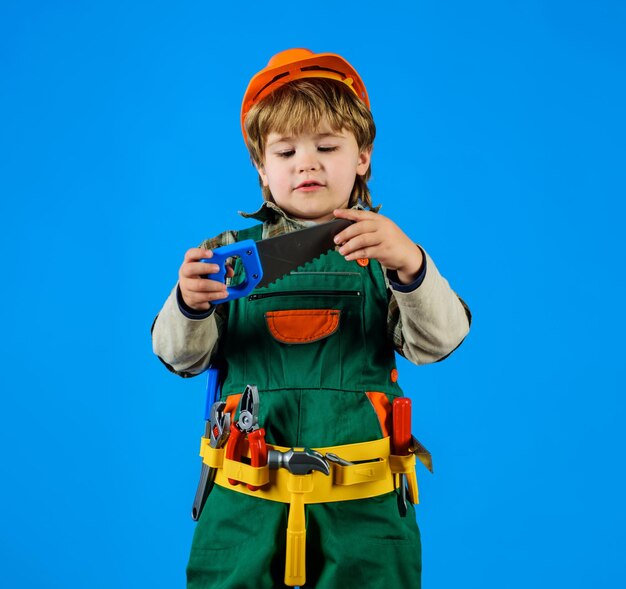 Niño con casco de seguridad y cinturón de herramientas con sierra trabajo con herramientas niño con uniforme de constructor con herramienta para