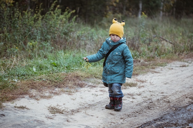 Niño caucásico en abrigo verde caminando en el campo, tiempo de otoño.