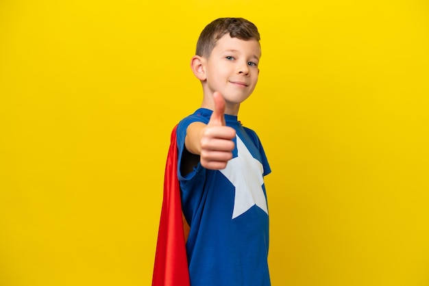 Un niño caucásico aislado de fondo amarillo disfrazado de superhéroe con el pulgar hacia arriba