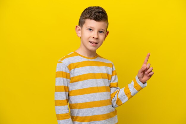 Un niño caucásico aislado de fondo amarillo mostrando y levantando un dedo en señal de lo mejor