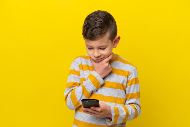 Foto un niño caucásico aislado de fondo amarillo pensando y enviando un mensaje