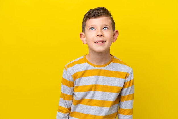 Un niño caucásico aislado de fondo amarillo pensando en una idea mientras miraba hacia arriba