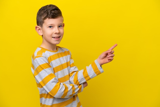 Un niño caucásico aislado de fondo amarillo señalando con el dedo hacia un lado