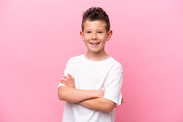 Un niño caucásico aislado de fondo rosa manteniendo los brazos cruzados en posición frontal