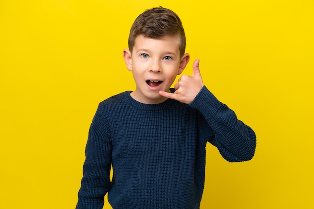 Niño caucásico aislado sobre fondo amarillo haciendo gesto de teléfono Llámame de nuevo firmar