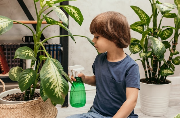 Un niño caucásico ayuda a rociar plantas en una habitación de la casa