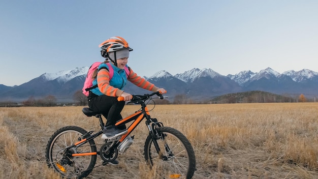 Un niño caucásico camina con bicicleta en el campo de trigo Niña pequeña caminando en ciclo naranja negro