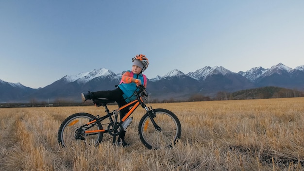 Un niño caucásico camina con bicicleta en el campo de trigo Niña pequeña caminando en ciclo naranja negro