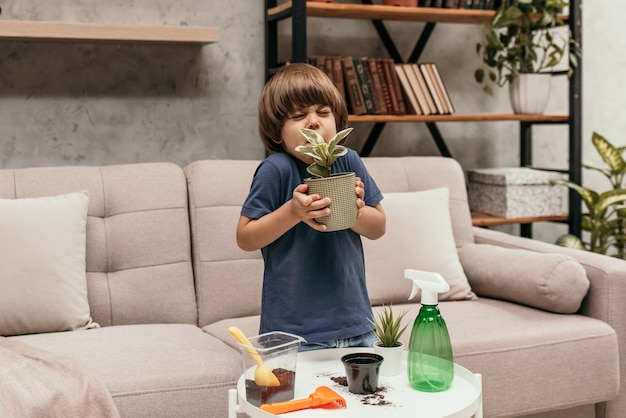 Un niño caucásico con una camiseta azul está sentado en el sofá y sosteniendo plantas dieffenbachia y estornudando