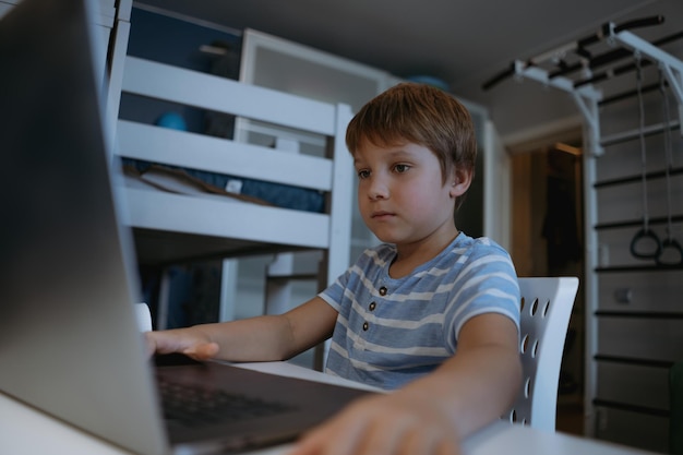 niño caucásico estudiando en casa escribiendo en su computadora portátil